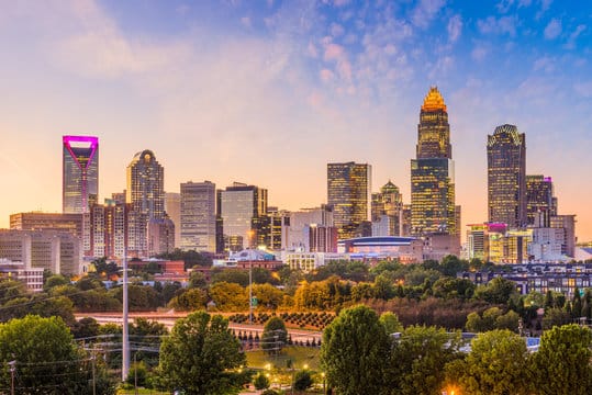 Skyline of a city with numerous skyscrapers during sunset, featuring a diverse range of building designs and surrounded by trees.